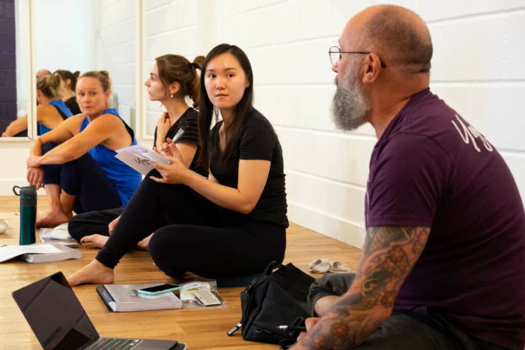 A picture of a Yoga teacher trainer offering a Yoga lecture to a group of yoga teacher trainees in Bristol