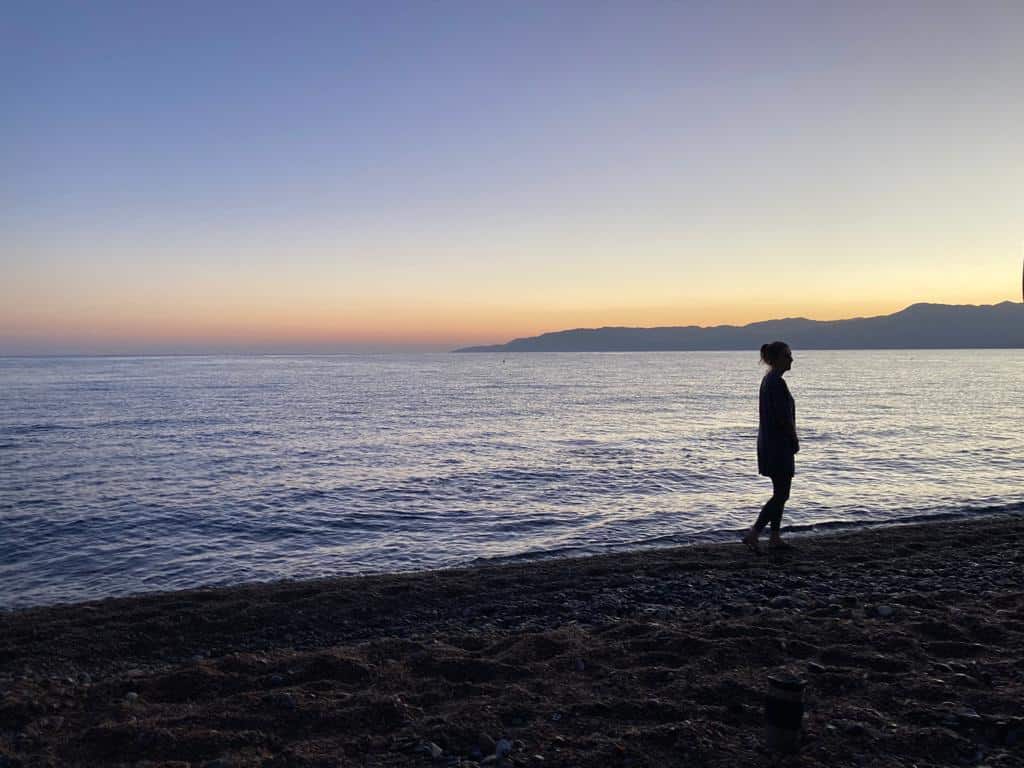 A woman walking along a beach in Cyprus on a yoga holiday at sunset.