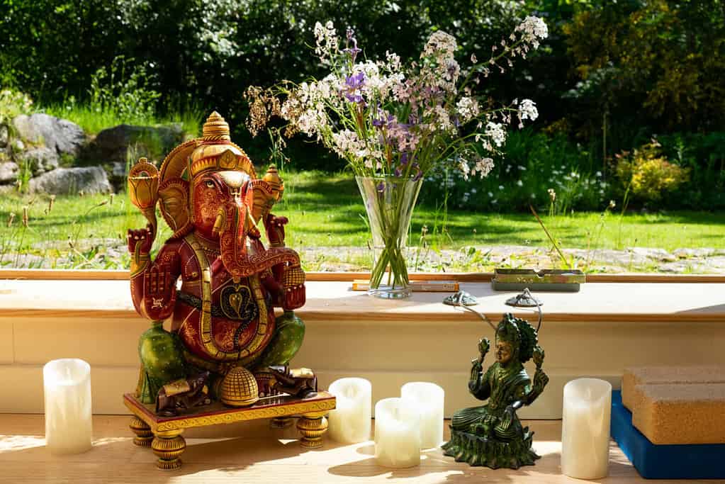 Statues of Ganesh and Lakshmi in the sunshine, surrounded by countryside, candles and flowers.