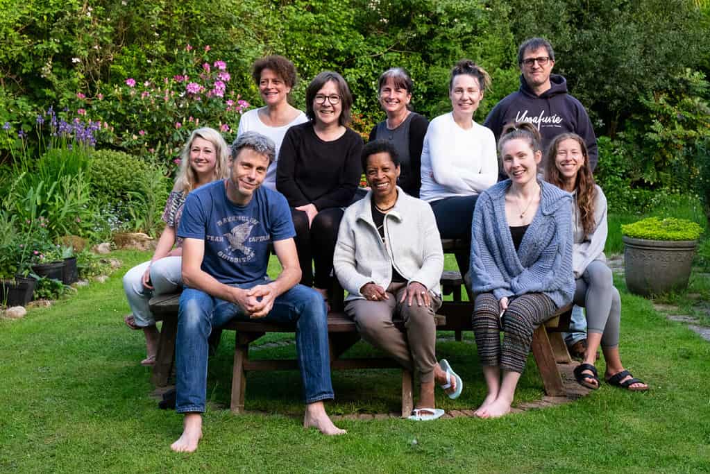 A group of people sat outside on a yoga retreat all sitting and smiling at the camera. They are in the countryside.